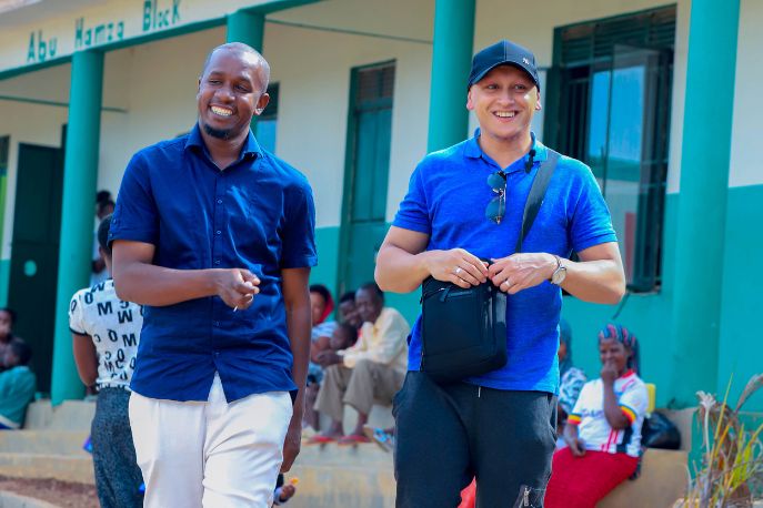 Two men walking together near a building, sharing a moment as they move along the path.
